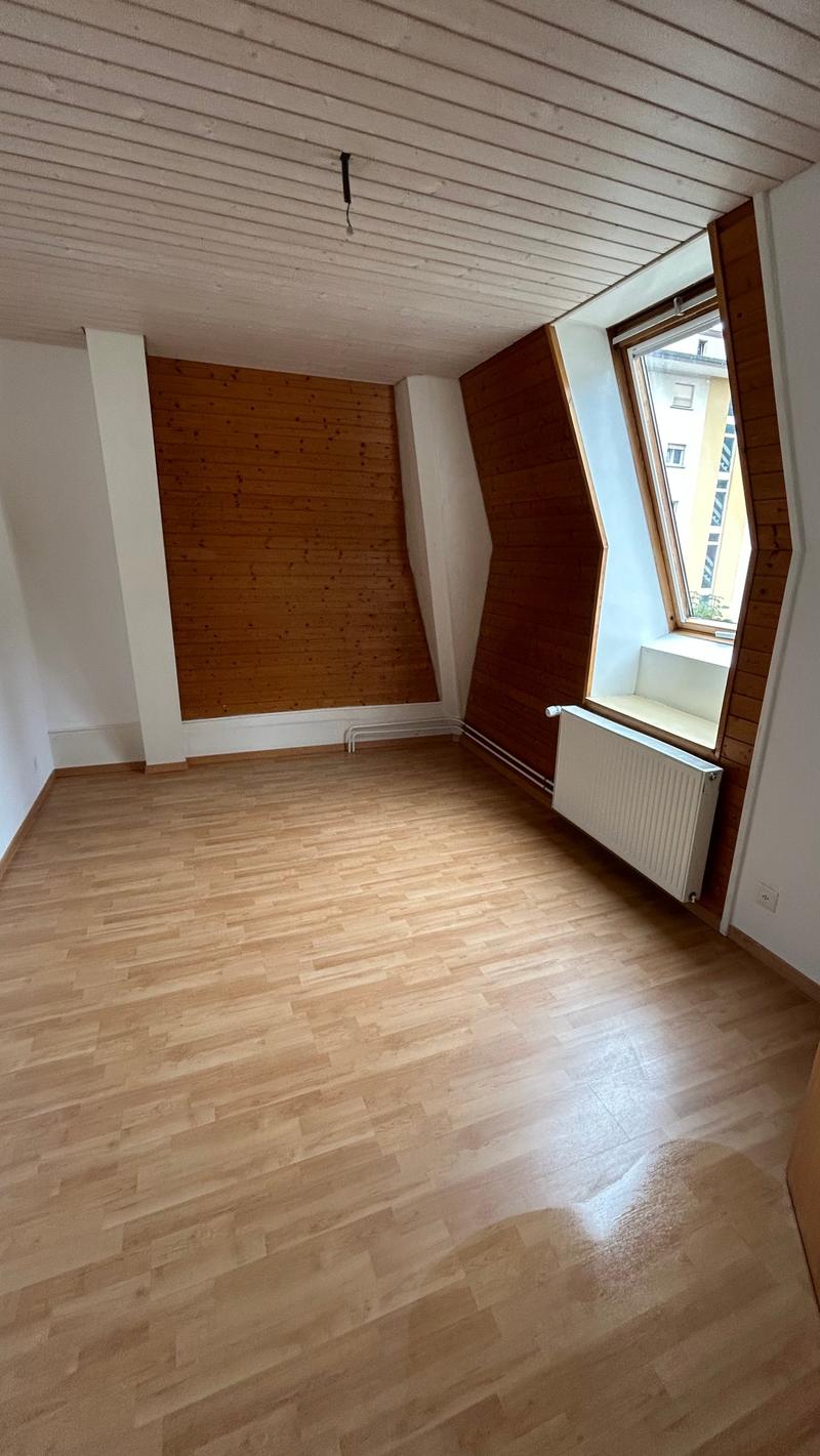 empty room with wooden floor, white walls, triangular window, wooden panels, radiator
