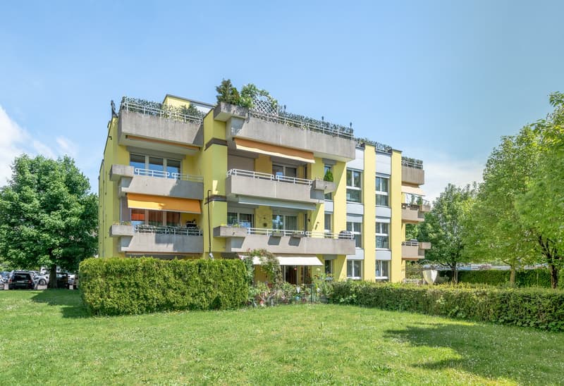 Yellow 4 story apartment building with multiple balconies, garden in front