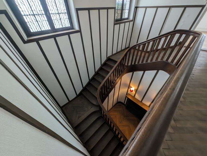 Spiral staircase with wooden handrails and steps, located in the middle of the house with decorative windows, lamp, and wooden flooring.
