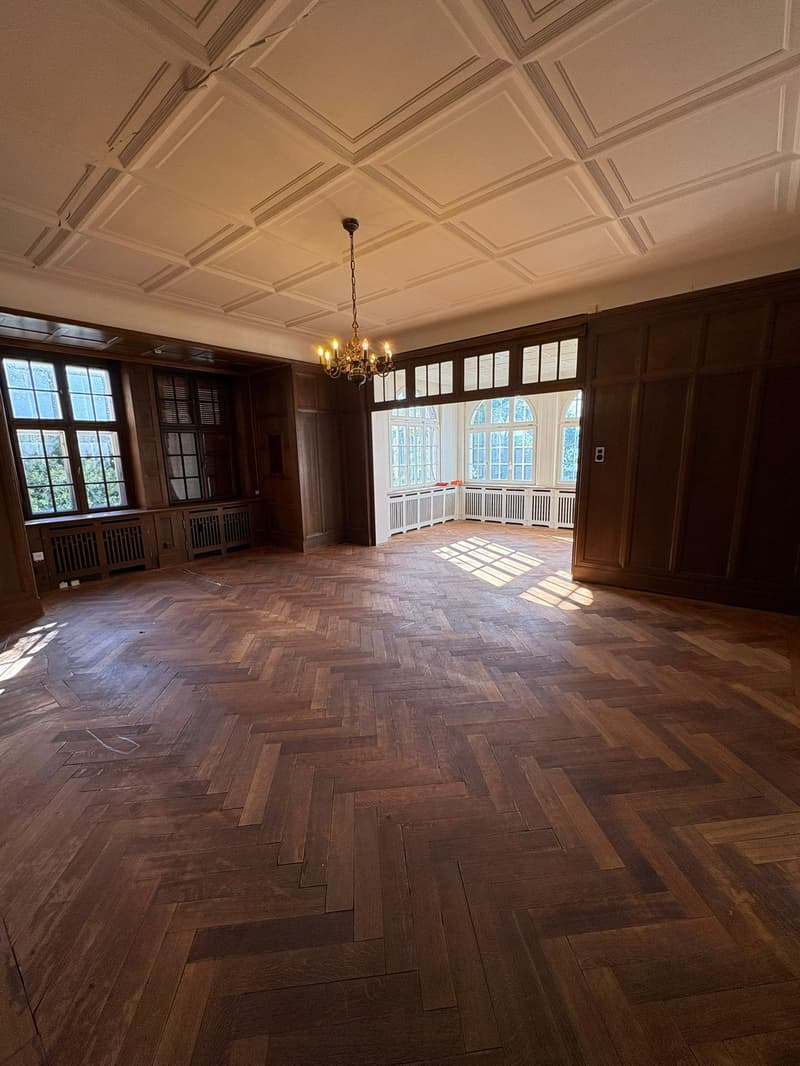 large room, wooden floor, chandelier, arched windows, wooden panels, white walls, warm lighting