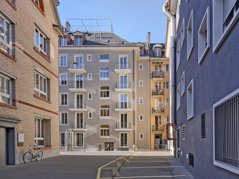 modern multi-story building with multiple balconies, brick facade, modern architectural design, parking area in front