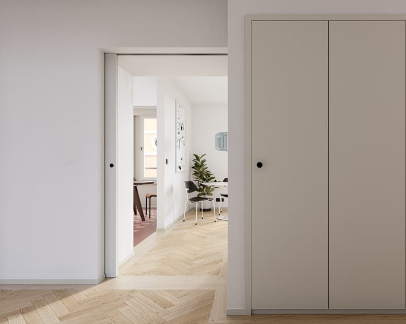 The image shows a hallway with a wooden herringbone floor, white walls, and a sliding door leading to another room. There is a potted plant on a chair in the adjacent room, and a dishwasher can be seen in the background.