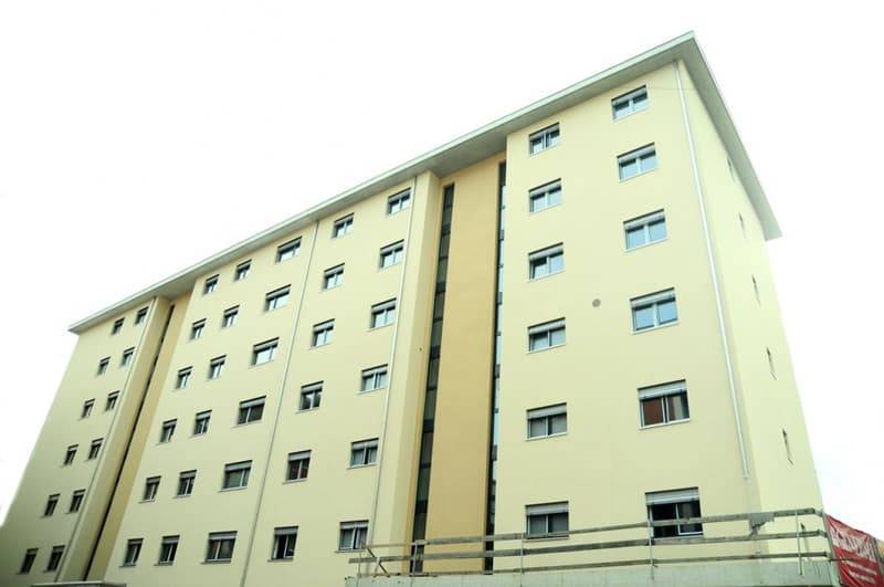 High-rise residential building with multiple floors, yellow exterior, numerous windows, some have curtains
