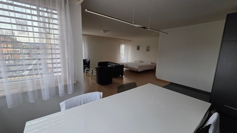 Living room with large windows, modern decor, wooden floor, two single beds, dining table and chairs, modern lamps