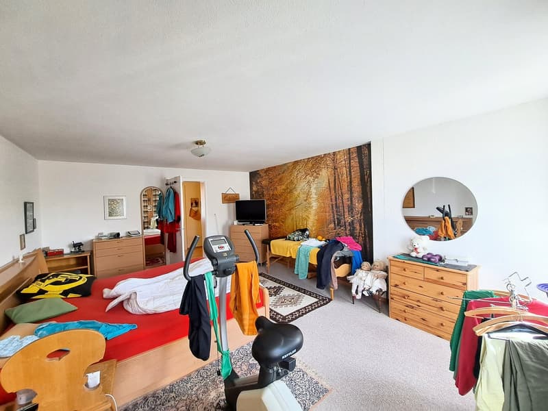 Spacious bedroom with hardwood floors, large wall mural depicting an autumn forest, exercise equipment, dresser, and various personal items and decor.