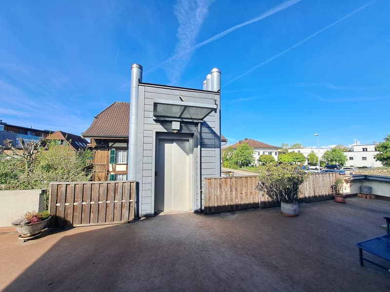 2-story house with gray siding, wooden fence, potted plants, and a balcony or terrace visible.