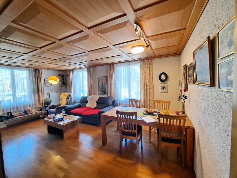 Spacious living room with wooden ceiling beams, hardwood floors, a fireplace, a sofa, a coffee table, and a dining table with chairs.