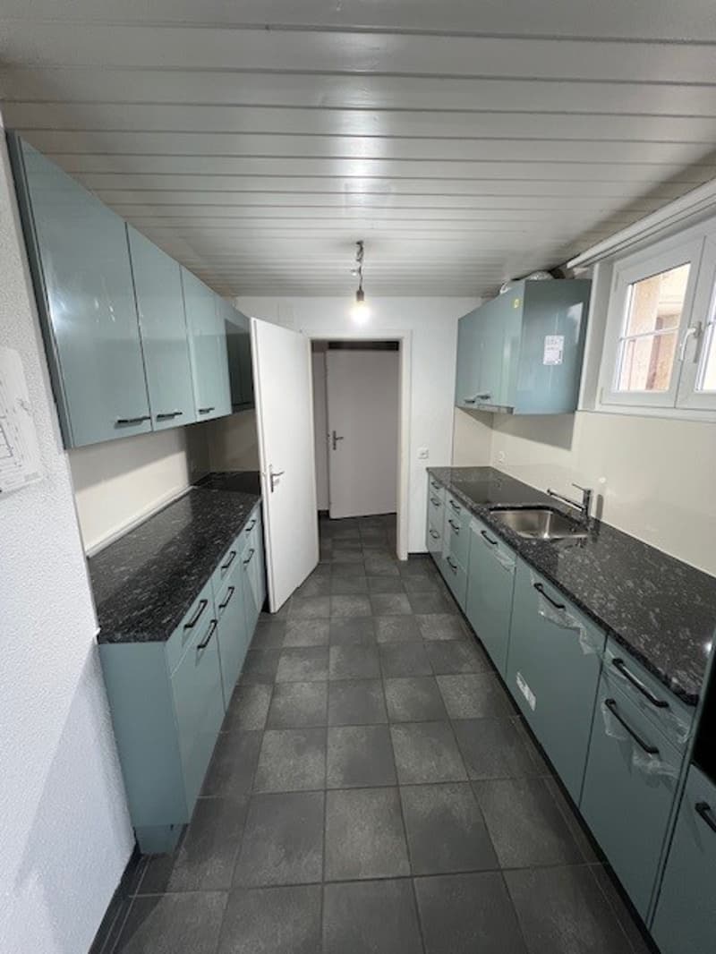 Empty kitchen with teal cabinets, granite countertop, stainless steel sink, faucet, cabinets, tiled floor, open door, windows
