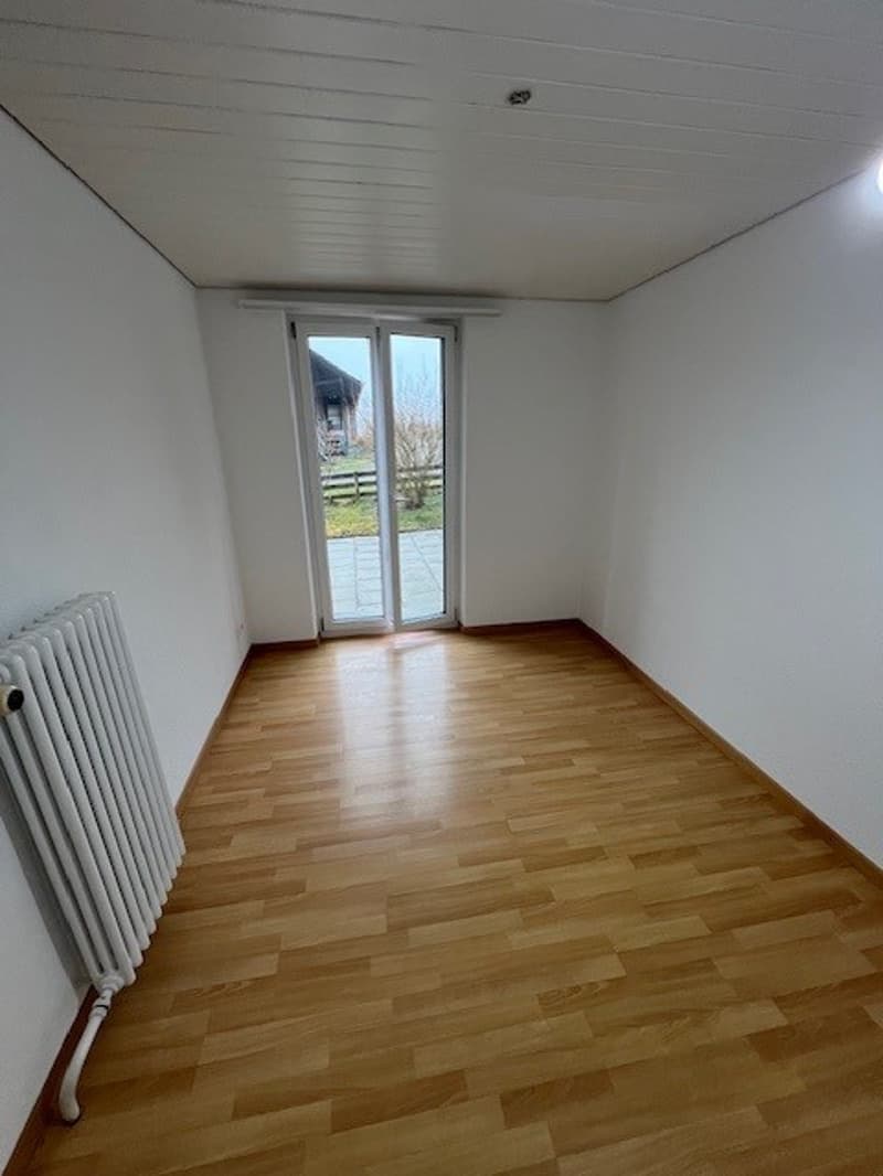 Empty room with white walls, wooden floor, radiator, sliding glass doors with an outside view