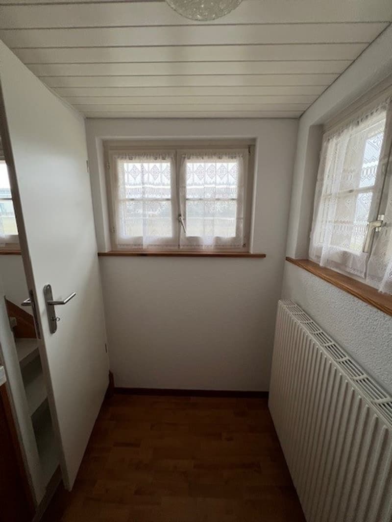 Empty room, white walls, windows with white curtains, wooden floor, white radiator