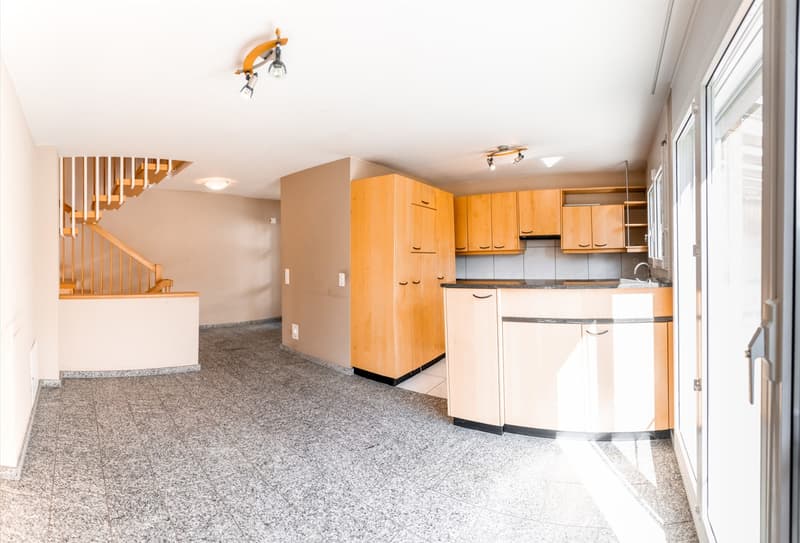 Empty kitchen with wooden cabinets, granite floor, and a staircase.