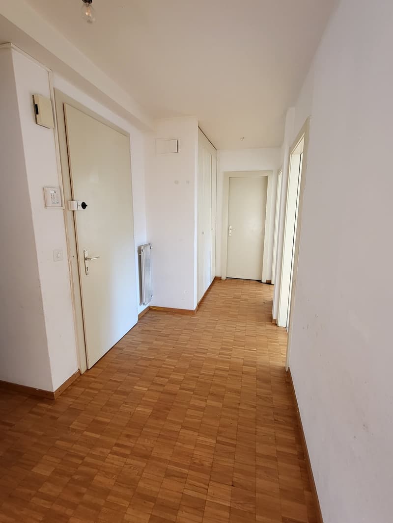 Empty corridor, wooden floor, white walls, 3 doors, 2 radiators