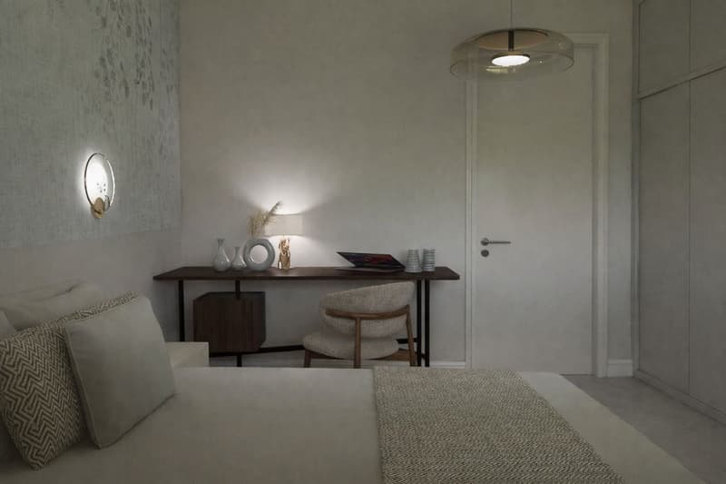 A bedroom with a bed, desk, chair, and decorative items. The room has white walls, a ceiling lamp, and a wall lamp. The bed has a white bedspread and pillows. The desk has a laptop, a lamp, and a vase. The chair is placed in front of the desk. The room ha