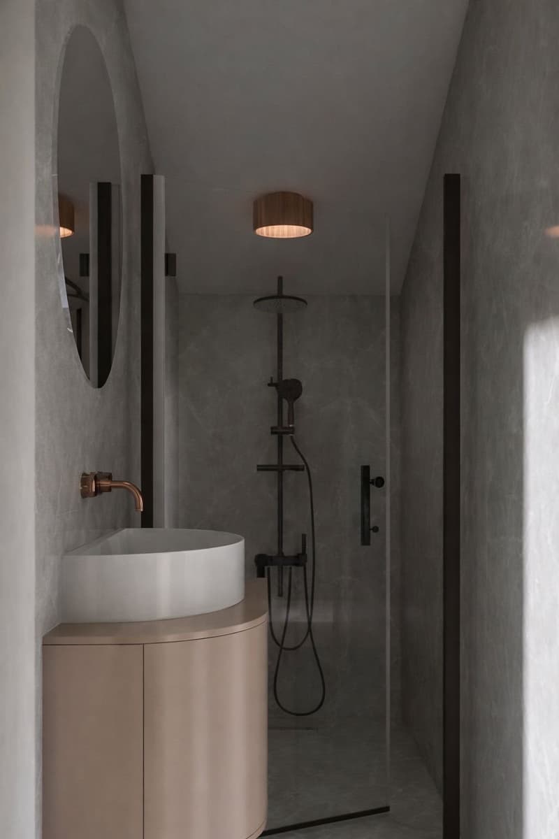 modern bathroom with a white sink, a round mirror, a shower with a shower head, and a wooden ceiling lamp