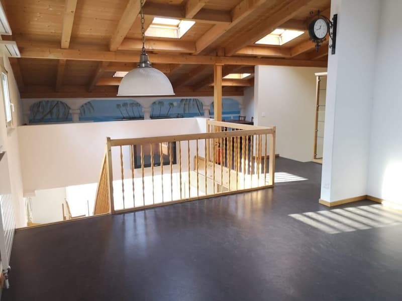 open room, wooden beams, black floor, wooden railing, hanging light, staircase, clock