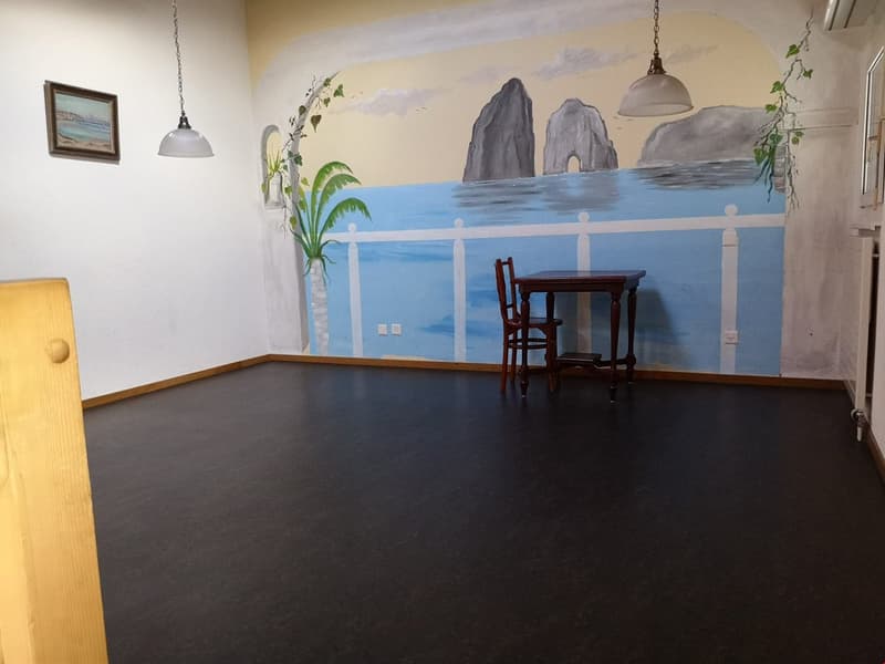 Empty room with beach-themed mural, wooden desk and chair, pendant lights, picture frame on wall, and outlet.