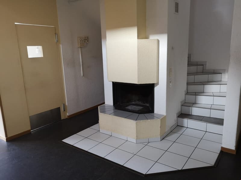 Room with white tiles, fireplace, staircase to upper floor, power outlet on wall, door with window.