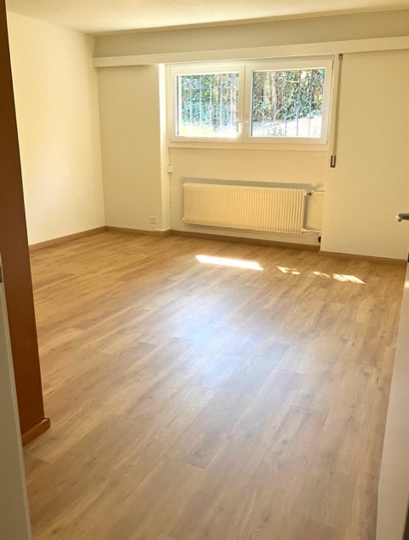 empty room with wooden floor, white walls, windows, and a radiator
