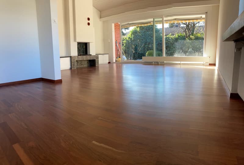 large room, hardwood floors, fireplace, large windows, view of trees