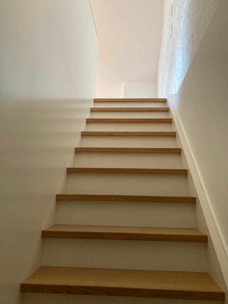 Wooden stairs with 10 steps leading up to a higher level. The stairs have a simple, minimalist design with clean lines and a light wood finish.