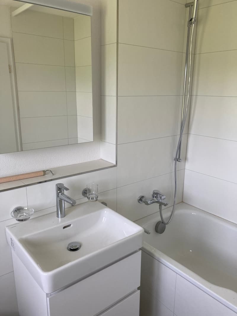 modern bathroom with a white bathtub, white sink, silver faucet, white tiles, large mirror and shower head