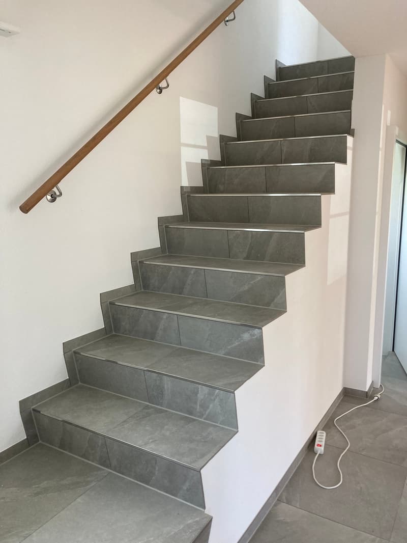 Modern staircase with grey tiles, wooden handrail