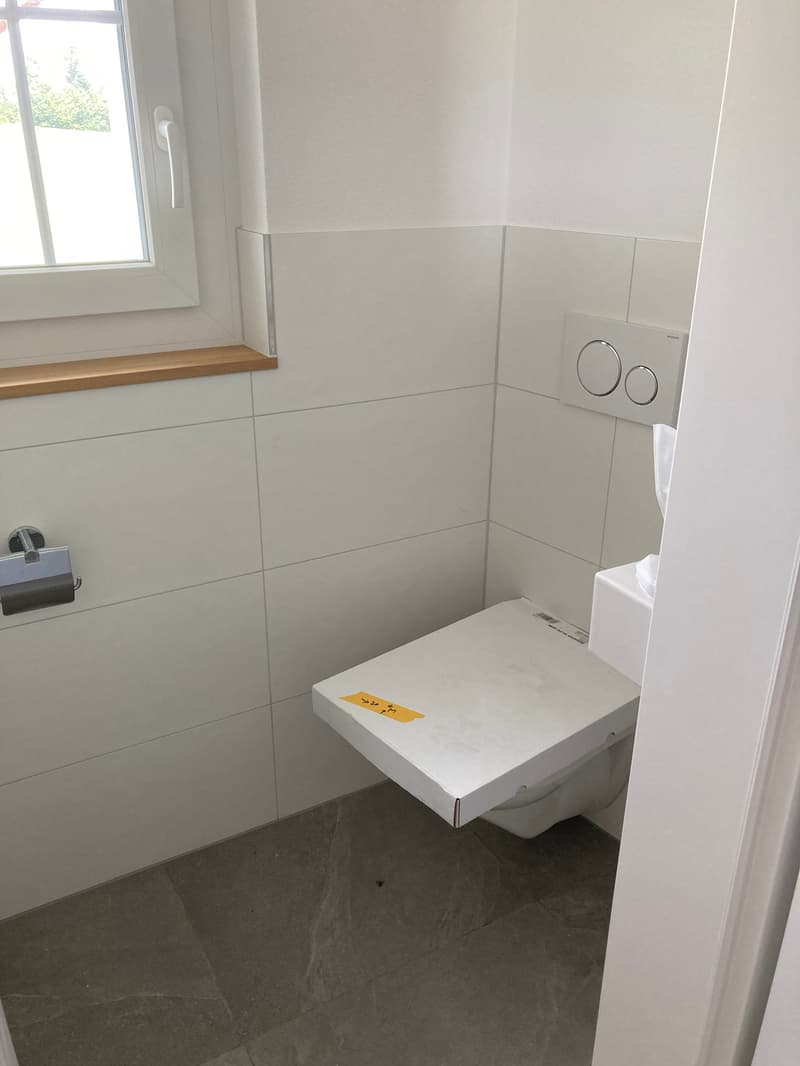 All white walls, corner mounted toilet, built-in toilet tank, window above toilet