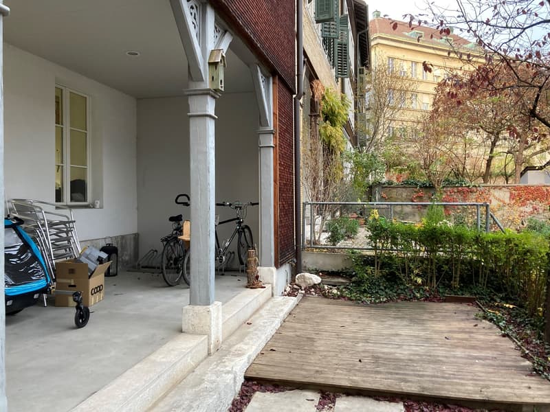 Exterior of a house with a wooden deck, bicycles parked, a box, and a birdhouse on the wall