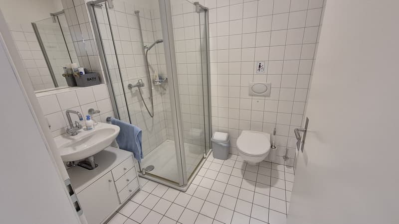 white tiled walls, white tiled floor, shower, sink, toilet, trash can, blue towel
