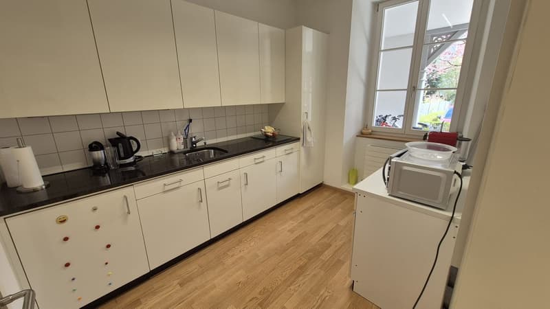 modern kitchen with white cabinets, black countertops, sink, faucet, microwave, dishwasher, coffee maker, paper towels, and a window