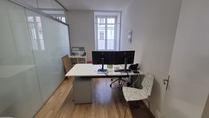 Desk with two monitors, chair, small cabinet, glass wall, wooden floor