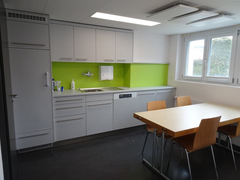 Modern kitchen with gray cabinets, green backsplash, stainless steel appliances, and a dining table with chairs.
