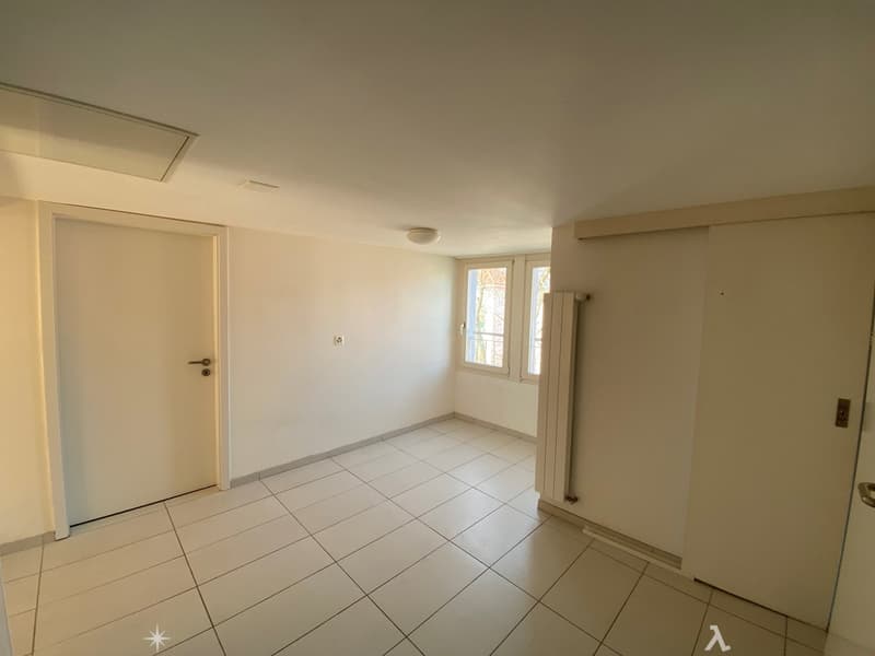 Empty room with white tiles, white walls, white doors, window with white frames, ceiling light, radiator