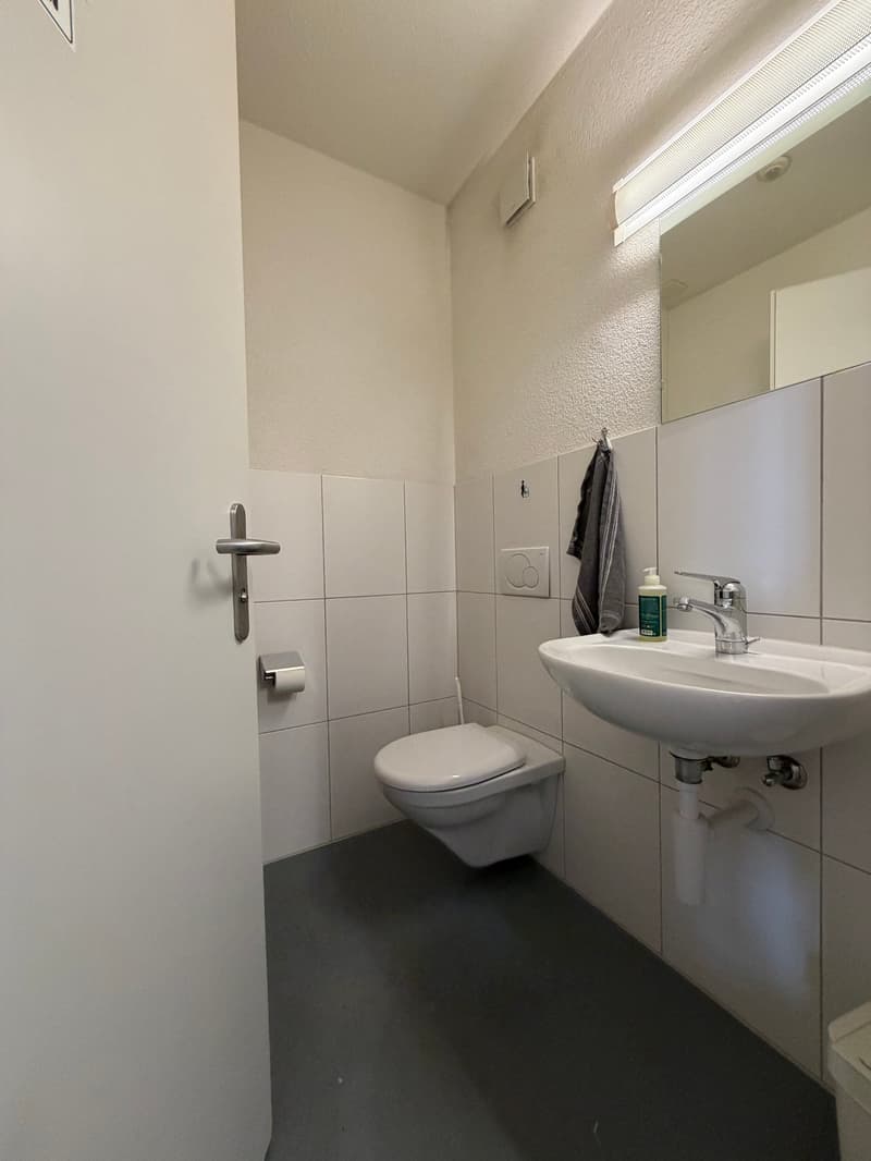 Modern bathroom with toilet, sink, and mirror. Tiled floor and walls.