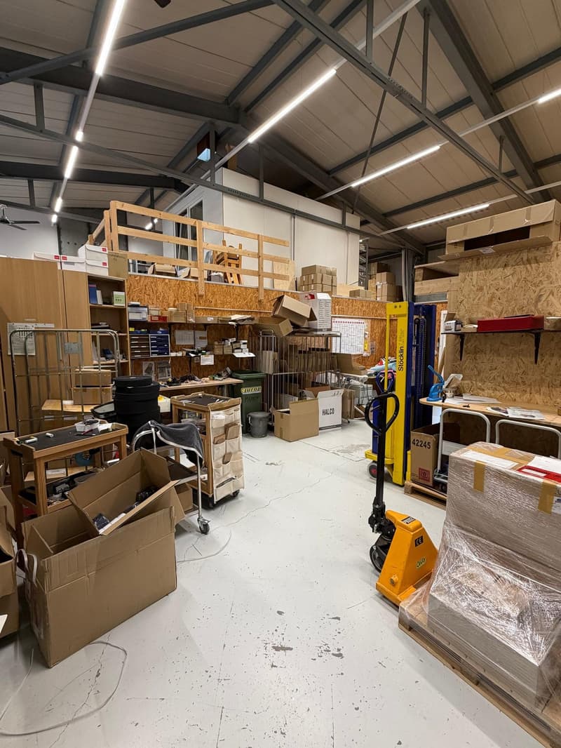 Warehouse interior with storage boxes, shelves, desks, carts, machines, and a clean floor