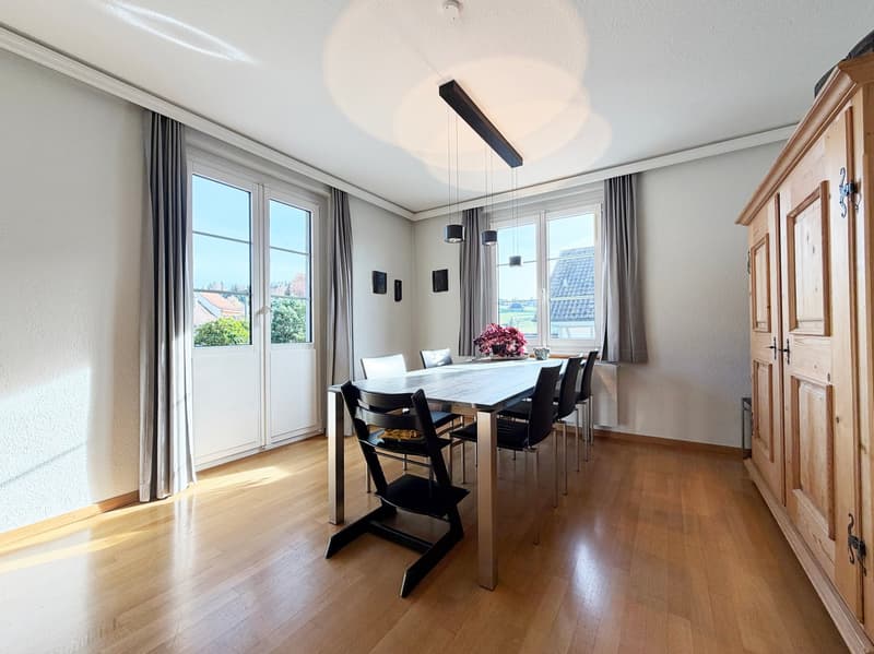 Dining room with a long dining table, modern style chairs, glass sliding doors leading to an outdoor space, ceiling lights, white walls, and wooden floor