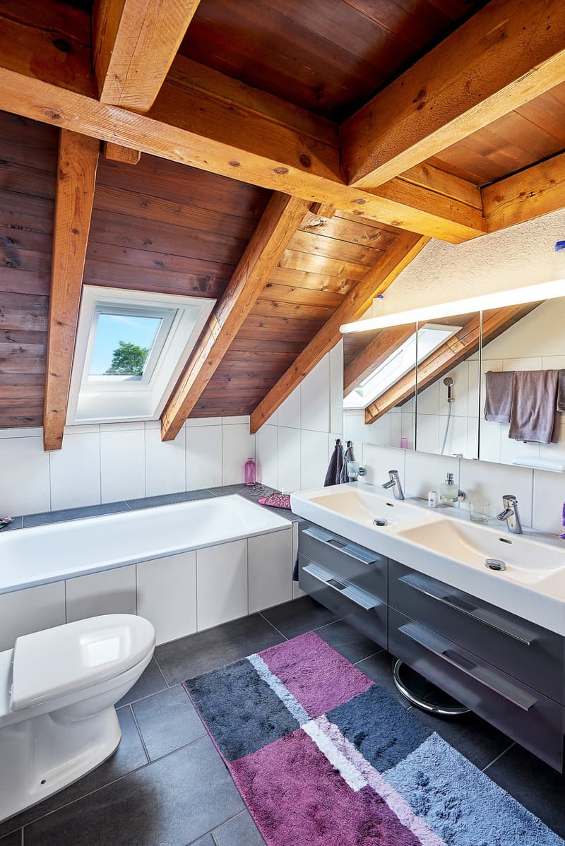 Bathroom with wooden ceiling, bathtub, double sink, toilet, skylight window, towel hanging