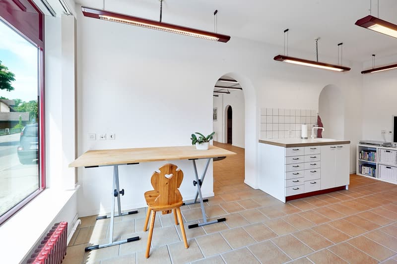 empty room with wooden desk, wooden chair, white kitchen and large window
