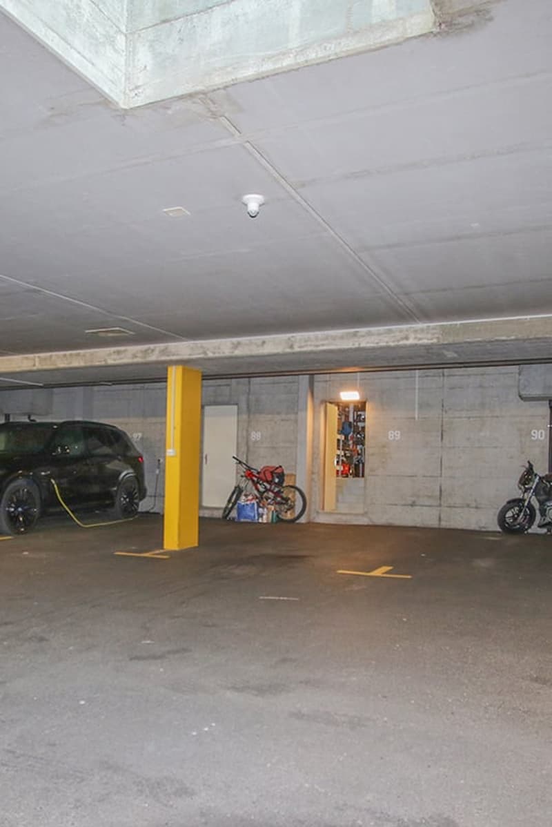 Empty parking garage with a yellow parking post, a black SUV, a red bike, and a blue motorcycle.