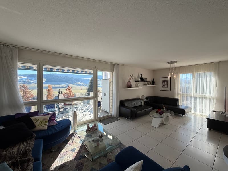 Spacious living room with balcony, large windows, white tile flooring, and a modern interior.
