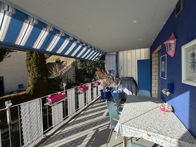 blue-walled terrace with retractable awning, metal railing, tables and chairs, blue pots, flower vase, lamp