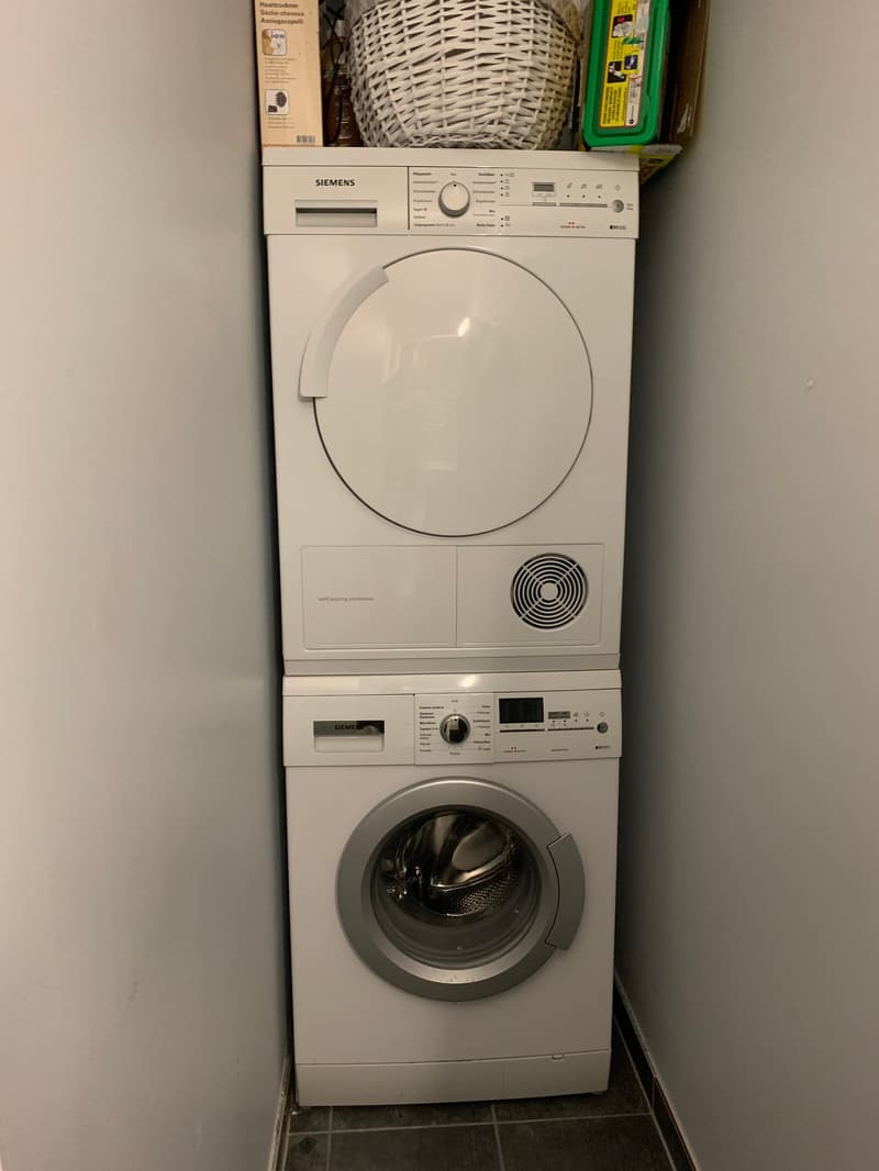 Stacked washing machine and dryer, Siemens brand, white, located in a corner of a room