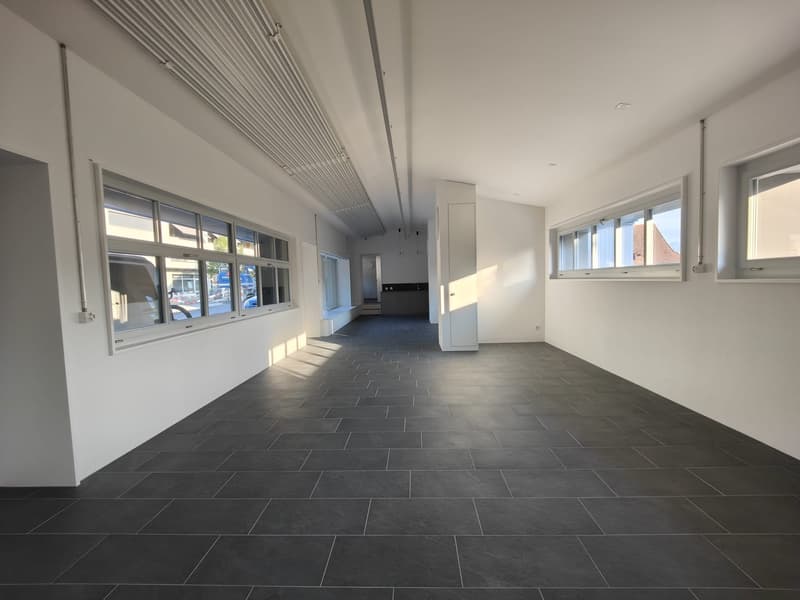 Empty room, with white walls and gray tile flooring, multiple windows, central heating duct