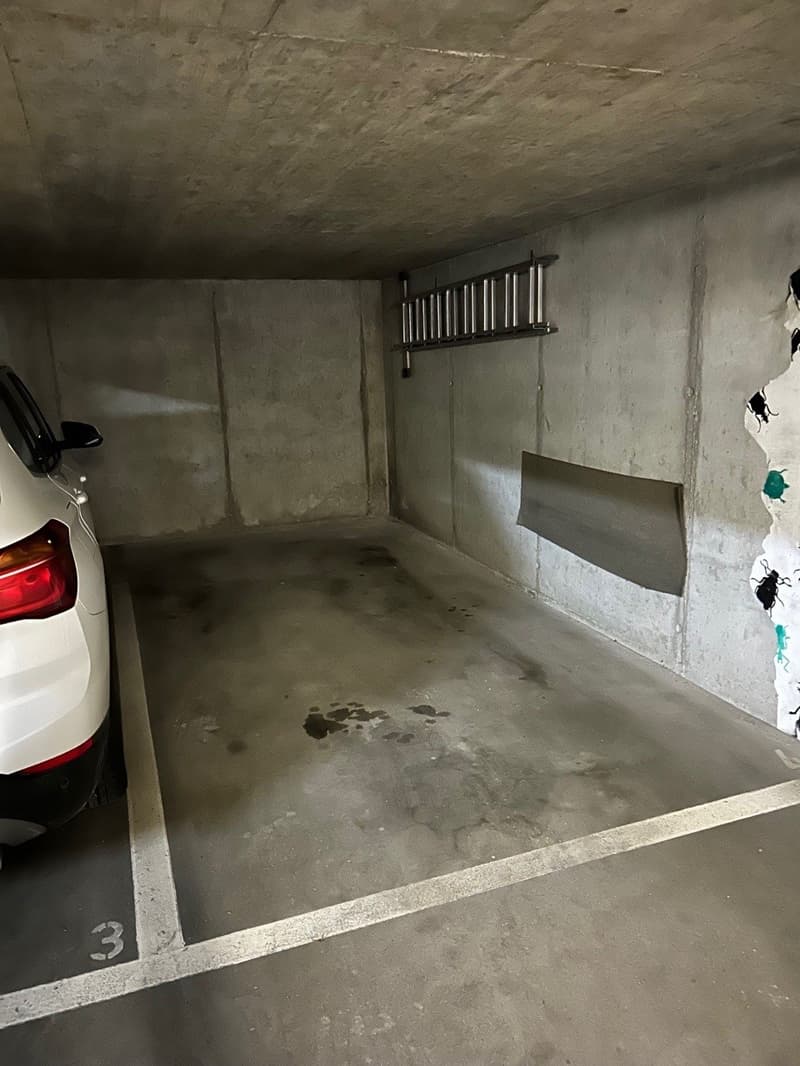 underground garage, a car parked, gray concrete floor and walls, small puddles on the floor