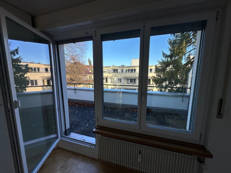A room with double doors opening to a balcony, windows facing the outside, white radiator below, and wooden floors.