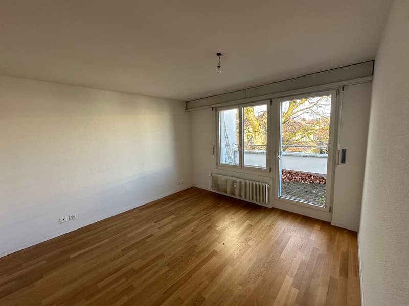 empty room with wooden floor, white walls, sliding glass door, balcony, radiator, natural light from outside