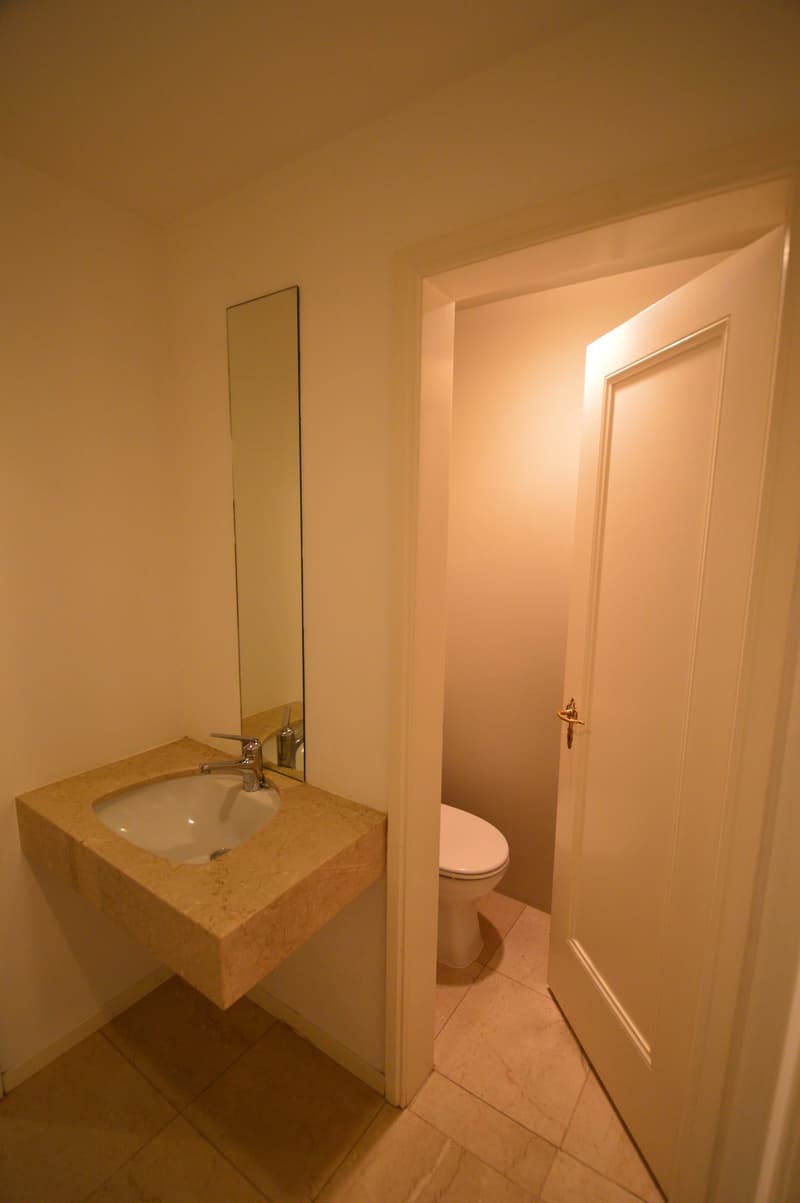 A small bathroom with a toilet, sink, and mirror on the wall. Tiled floor.