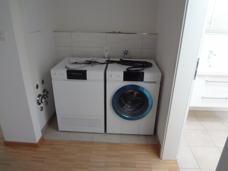 A laundry room with two white machines in a corner. One is a washing machine, the other is a dryer.