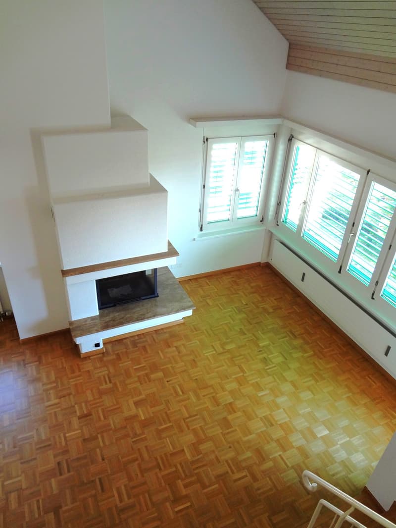 Spacious living room with hardwood flooring, white walls, large windows, and a fireplace feature.