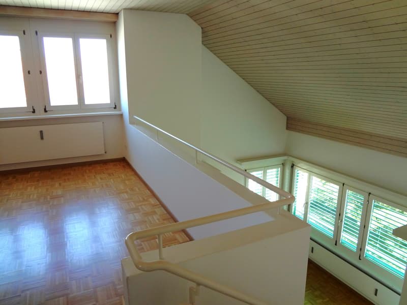 Attic room with slanted ceiling, wooden paneled walls, large windows, hardwood floor, and a railing along the upper level.